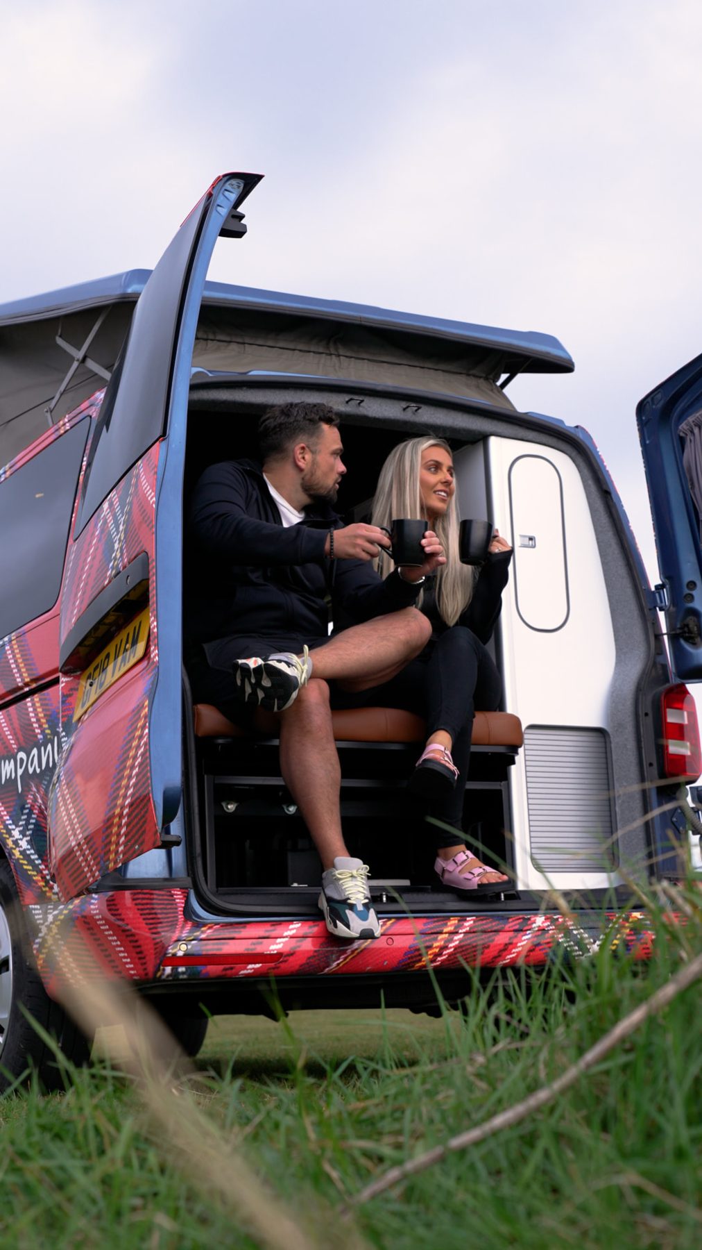 A couple enjoying coffee in the back of a branded camper van
